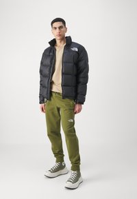 Sort dunjakke med høj krave, beige sweatshirt, grønne sweatpants og grønne høj-top sko. Logoer vises på tøj.