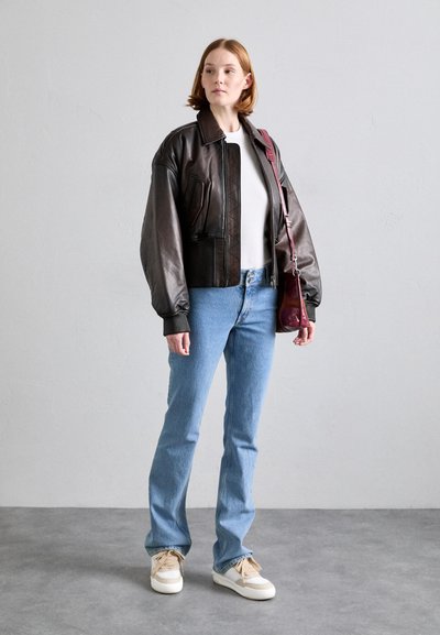 Brown leather bomber jacket with ribbed cuffs, white top, light blue straight-leg jeans, and cream sneakers, holding a burgundy bag.