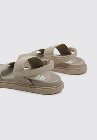 Sandalias color caqui con amplias correas de textil y una suela de goma contorneada. La plantilla muestra texto blanco y tiene un acabado suave.