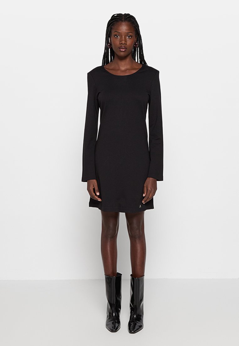 Czarna sukienka z długimi rękawami, okrągłym dekoltem i dopasowanym krojem. Wykonana z gładkiego materiału, zestawiona z błyszczącymi, wysokimi botkami do kolan.