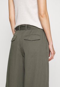 Olive green wide-leg trousers with a smooth texture, featuring two back pockets and a belt loop waistband, styled with a light knitted top.