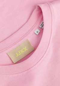 Κοντινό πλάνο ροζ T-shirt με στρογγυλή λαιμόκοψη που δείχνει μπεζ ετικέτα μάρκας JJXX και μικρό ταμπελάκι μεγέθους S μέσα στη γιακά.