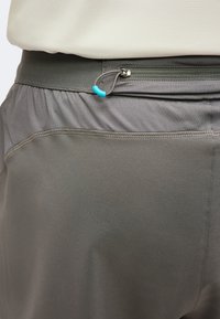 Gros plan sur un pantalon de sport gris avec une taille élastique et une petite poche zippée dotée d'une tirette bleue.