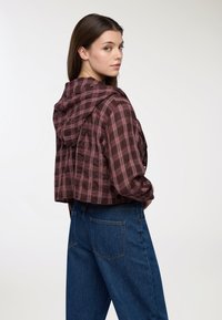 Felpa corta a quadri bordeaux con finitura testurizzata, dotata di cappuccio con cordini e vestibilità casual, abbinata a jeans in denim blu a vita alta.