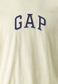 Světle žluté bavlněné tričko s nápisem "GAP" vyšitým tmavě modrými písmeny. Jemná textura, volný střih a standardní kulatý výstřih.
