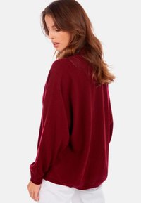 Pull en maille bordeaux à manches longues et coupe décontractée. Doté d'un col rond simple et d'une texture douce. Associé à un pantalon blanc.