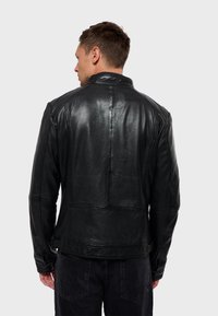 Chaqueta de cuero negra con una textura suave, collar estructurado y detalles en las costuras. Presenta un diseño ajustado y una forma definida.