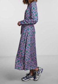 Klänning med långa ärmar i en grön och rosa abstrakt mönster, knä-lång, i lätt tyg, kombinerad med flerfärgade sportskor.