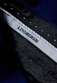 Czarna tkanina o fakturowanym wykończeniu, z białą metką z napisem "LINDENBERGH" i starannym przeszyciem wzdłuż krawędzi.