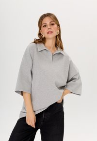 Grijze oversized polo met korte mouwen, voorzien van een kraag en een zachte textuur, gecombineerd met zwarte spijkerbroek.