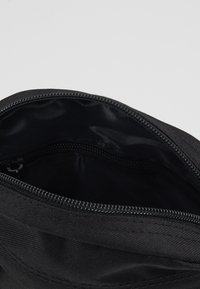 Borsa in tessuto nero con apertura a zip, caratterizzata da un rivestimento interno liscio. L'esterno presenta una texture sottile e nessun motivo visibile.