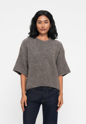 Brun tekstureret striktrøje med korte ærmer og rund halsudskæring, parret med mørke jeans. Simpelt, afslappet design med en løs pasform.