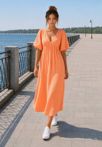 Jeune femme marchant sur une promenade au bord de l'eau, portant une robe midi orange et des baskets blanches sous un ciel clair.