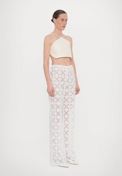 Off-white crop top met dunne bandjes, gecombineerd met sheer witte broek met een diamanten patroon, en puntige hakken. Gladde textuur.