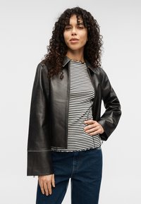 Μαύρο δερμάτινο μπουφάν με γιακά, φερμουάρ κλείσιμο και μακριά μανίκια. Συνδυασμένο με ριγέ μπλούζα με στρογγυλή λαιμόκοψη και τζιν παντελόνι. Λείο ύφασμα.