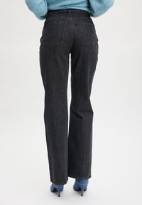 Jeans noirs taille haute avec une silhouette droite, dotés de deux poches arrière et d'une finition en denim texturé. Associés à des escarpins bleus.