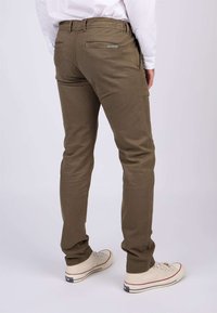 Pantalon en tissu kaki à coupe slim, avec une taille mi-haute, deux poches arrière et un accent de logo. Associé à des baskets blanches.