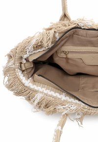 Beżowa pleciona torba z frędzlami. Wnętrze wyściełane, wyposażone w kieszeń na suwak oraz dodatkową kieszeń otwartą. Gładka faktura i rączka zrobiona z liny.