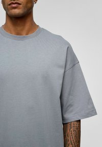 Lichtgrijze t-shirt met een ronde halslijn en korte mouwen, met een gladde textuur en een ontspannen pasvorm. Accenten van zichtbare stiksels.