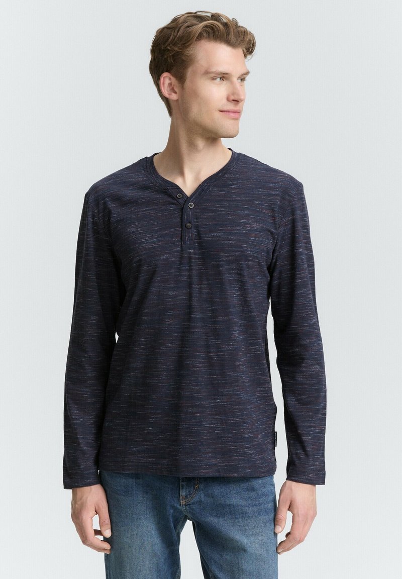 Marineblå langærmet henley skjorte med et struktureret mønster, tre-knap placket og kontrasttråd detaljer, parret med blå jeans.