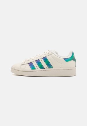 Zapatillas de cuero blanco con rayas iridiscentes en verde y azul, suela de goma texturizada y punta redondeada. Fusión de elementos de diseño clásicos y modernos.