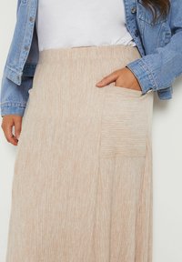 Jasno beżowa spódnica do kolan wykonana z prążkowanej tkaniny, z boczną kieszenią i elastycznym paskiem w talii. W połączeniu z dżinsową kurtką.