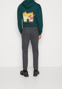 Zielona bluza z kapturem z grafiką frytek i logo MTV na plecach, w połączeniu z szarymi spodniami w paski i czarnymi sneakersami.