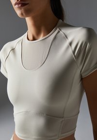 Light beige athletic top made of smooth, stretchy fabric. Features a round neckline, short sleeves, and seam detailing.