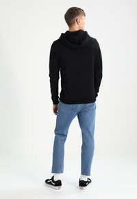 Felpa nera con cappuccio, in misto cotone, con polsini e orlo a costine, abbinata a jeans azzurri chiari e sneaker nere con dettagli bianchi.