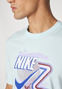Camiseta de algodón azul claro con un gran logo de "NIKE" en blanco y azul, con acentos gráficos coloridos y un cuello redondo.