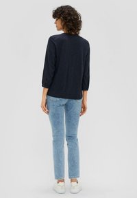 Marineblaue, langärmlige Hemd mit hochgekrempelten Ärmeln, aus leichtem Material und entspannter Passform. Kombiniert mit hellblauen Jeans und weißen Sneakern.