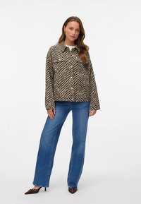 Bruin en beige gestreept jasje met knoopsluiting, twee borstzakken en een losse pasvorm, gecombineerd met wijde blauwe jeans en puntige schoenen.