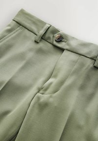 Light green trousers with a flat front design, featuring a single button closure and side pockets, made of smooth fabric.