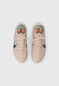 Ζευγάρι ροζ πλεκτών αθλητικών παπουτσιών με μαύρα λογότυπα swoosh και λευκές κορδόνες, από πάνω σε λευκό φόντο.