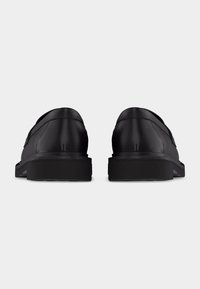 Ζευγάρι μαύρα δερμάτινα επίσημα παπούτσια, φαίνονται από πίσω, πάνω σε απλό ανοιχτό γκρι φόντο.