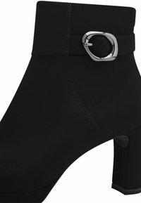 Svart ankelboot med klack, tillverkad av mjukt material. Har en glänsande silverfärgad spänne på sidan och en slät yta med sömmar.