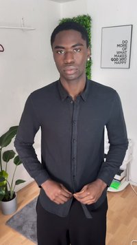 Camicia nera con bottoni, maniche lunghe e una consistenza morbida. La camicia presenta un colletto ed è indossata con la parte anteriore parzialmente infilata nei pantaloni.