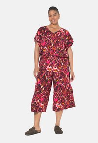 Multikleurige outfit met een losse, kortekous top en wijde capri-broeken in een abstract patroon van roze, rood en zwart. Zachte stof.