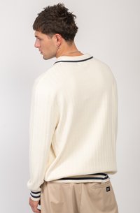 Suéter ribeteado crema con un cuello y detalles en azul marino. Presenta un corte holgado y mangas largas. Textura suave. Combinado con pantalones beige claros.
