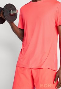 Růžové sportovní tričko s texturovanou tkaninou, kulatým výstřihem a krátkými rukávy, spárované s odpovídajícími šortkami s logem na lemu.