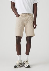 Shorts din denim bej cu un croi clasic, buzunare frontale și tiv cusut. Purtați cu un tricou alb simplu și adidași gri de alergare.