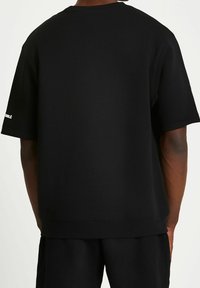 Black cotton oversized t-shirt with a round neckline, short sleeves, and a straight hem. Features logo detail on the sleeve.