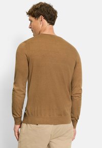 Brauner Strickpullover mit Rundhalsausschnitt, langen Ärmeln und seitlichem Schlitz am Saum. Weicher Stoff, taillierte Silhouette und nahtloses Schulterdesign.