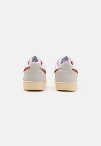 Sportsko sko med grå suede bak, hvite sidepaneler, røde detaljer og beige gummisåle. Med polstret krage og minimalistisk design.