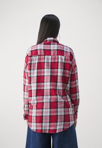 Chemise à carreaux rouge et noire avec des manches longues, des poignets boutonnés, un col rentré et un empiècement au dos. Tissu doux avec une coupe décontractée.