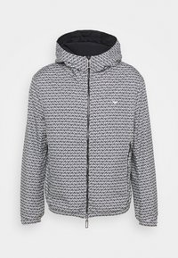 Vaddernad jacka med huva, med ett svart och vitt geometriskt mönster, dragkedjestängning och elastiska manschetter. Mjuk, texturerad tyg.