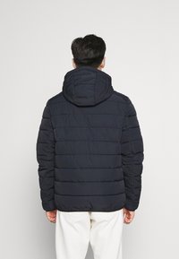 Doudoune marine avec capuche, présentant des sections matelassées, une fermeture éclair à l'avant et des manches longues. Le matériau semble lisse avec un design léger.