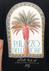 Εικονογράφηση ενός κόκκινου φοίνικα, πλαισιωμένου από διακοσμητικό μωσαϊκό πλαίσιο με κείμενο "PALAZZO DELLE ROSE" και ιταλική διεύθυνση από κάτω σε μαύρο ύφασμα.