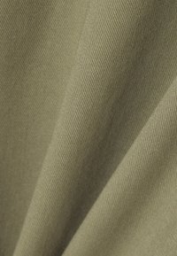 Gros plan sur un tissu beige avec une texture en tissage diagonal et des plis doux créant des ombres et de la profondeur.