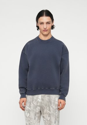 Tumed sweatshirt ümaralt kaeluselt, langevate õlgadega ja soonikkoes mansettidega; kangas näib pehme ja siledat tekstuuri omav.